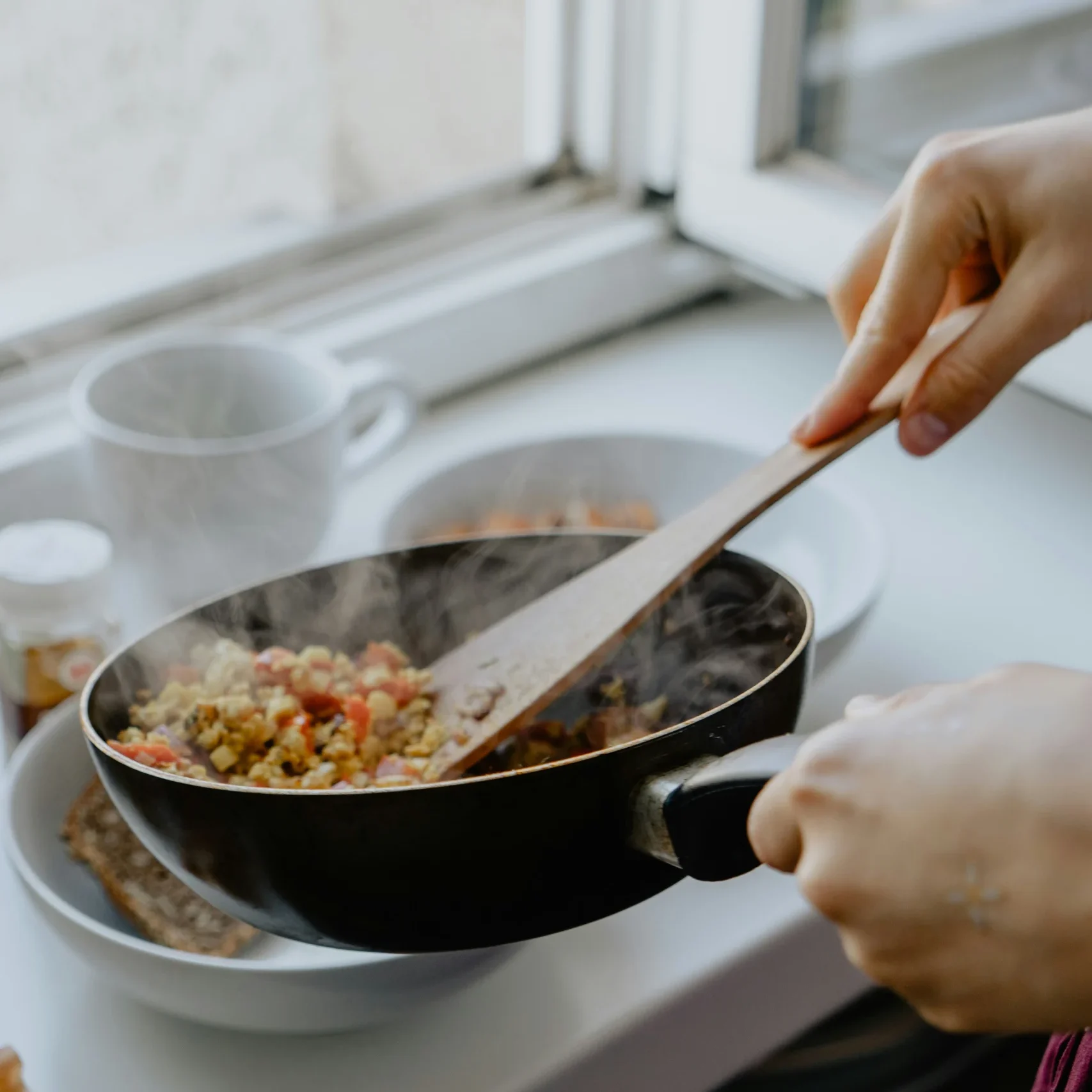 Person cooking scrambled eggs in a black pan.